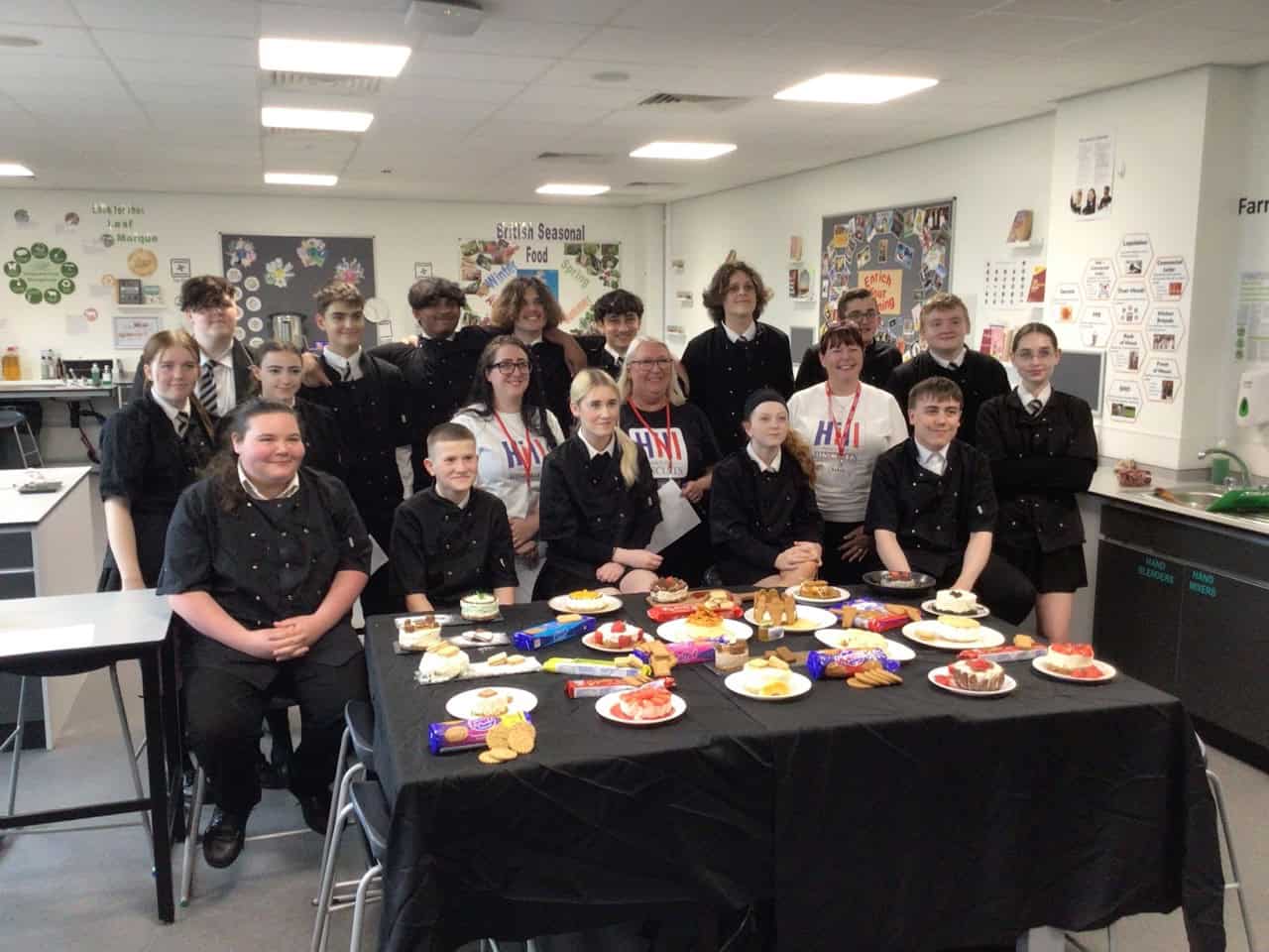 Laurus Ryecroft students and Hill Biscuits staff gather around a table of their homemade cheesecakes.